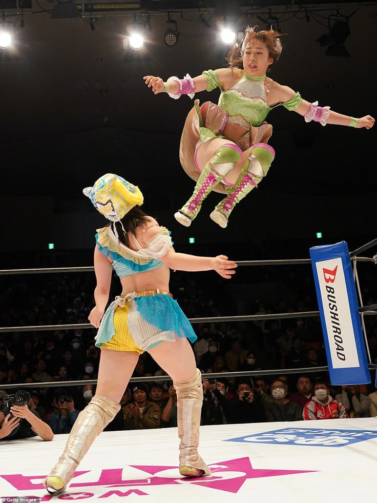 two women in costumes are performing on the stage while people watch from the stands behind them