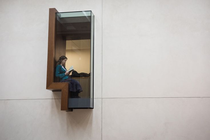 a woman sitting on a ledge reading a book in an office building's window