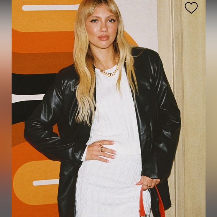 a woman standing in front of a wall holding a red purse and wearing a black leather jacket