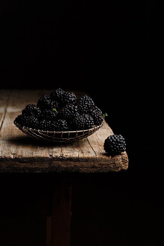 blackberries sit in a basket on a wooden table, ready to be picked up