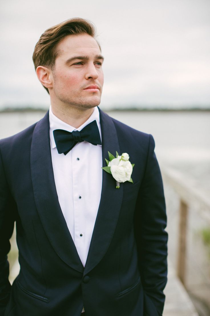 a man in a tuxedo and bow tie standing on a pier looking off into the distance