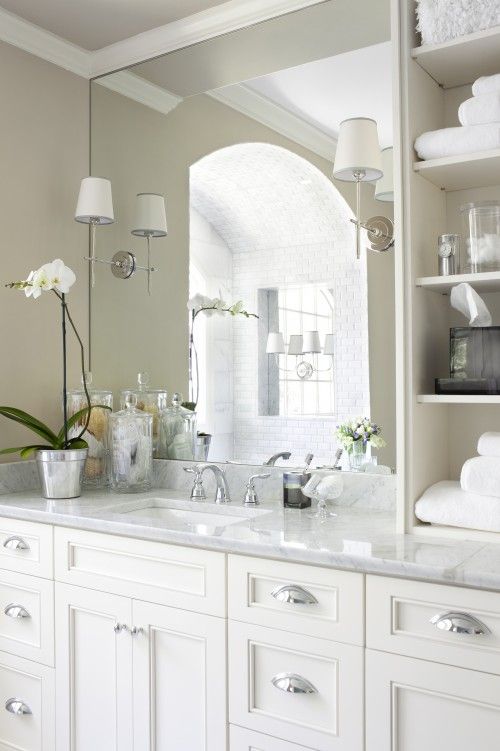 a bathroom with white cabinets and marble counter tops in front of a large mirror above the sink