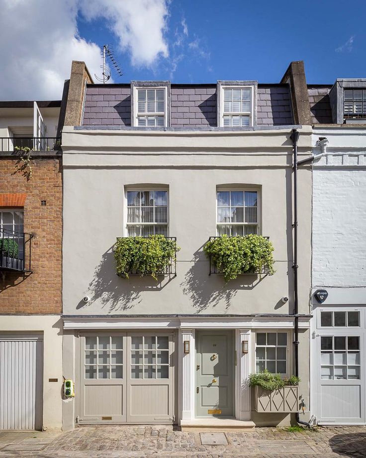 two story white building with three windows and plants on the top floor in front of it