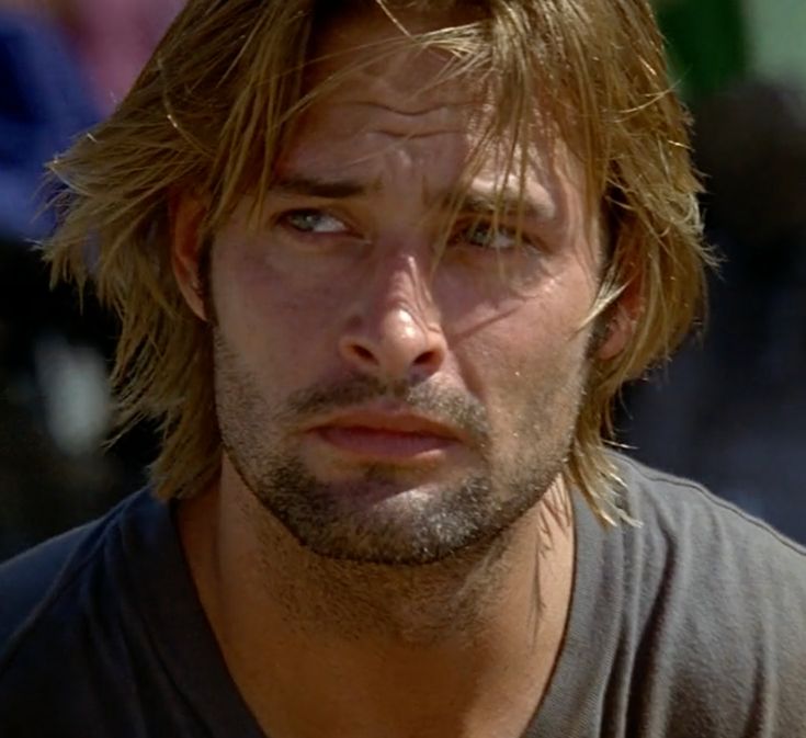 a close up of a person wearing a black shirt and long blonde hair with a serious look on his face