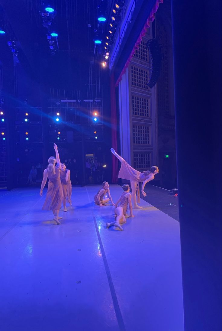 dancers performing on stage in front of an audience at a show with blue lighting and chandeliers