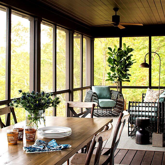 a wooden table sitting on top of a porch next to a tall window filled with lots of windows