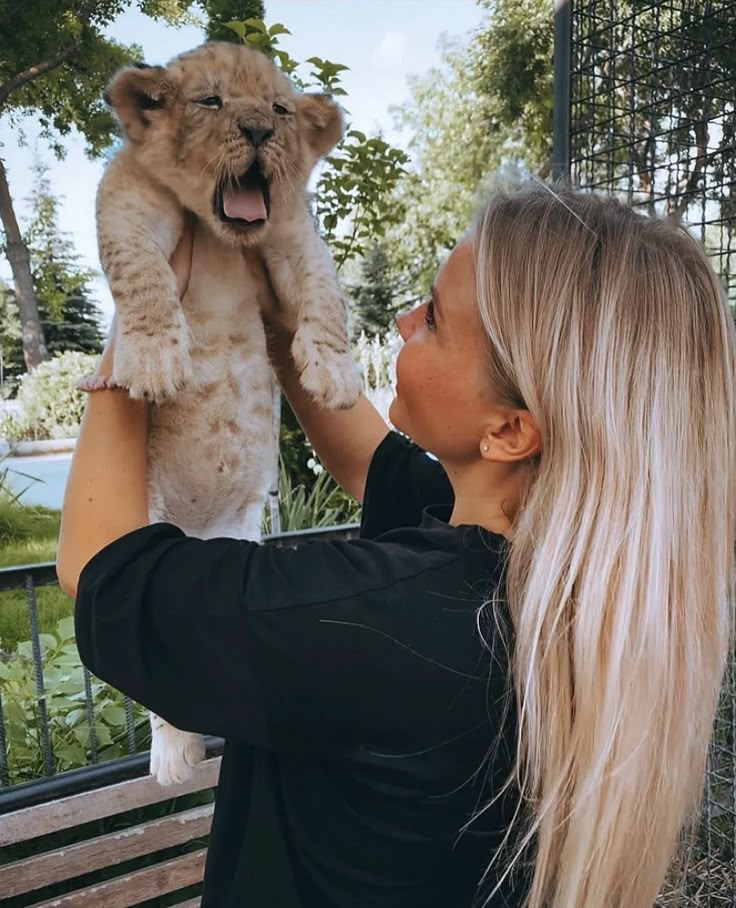 a woman holding a baby lion up to her face