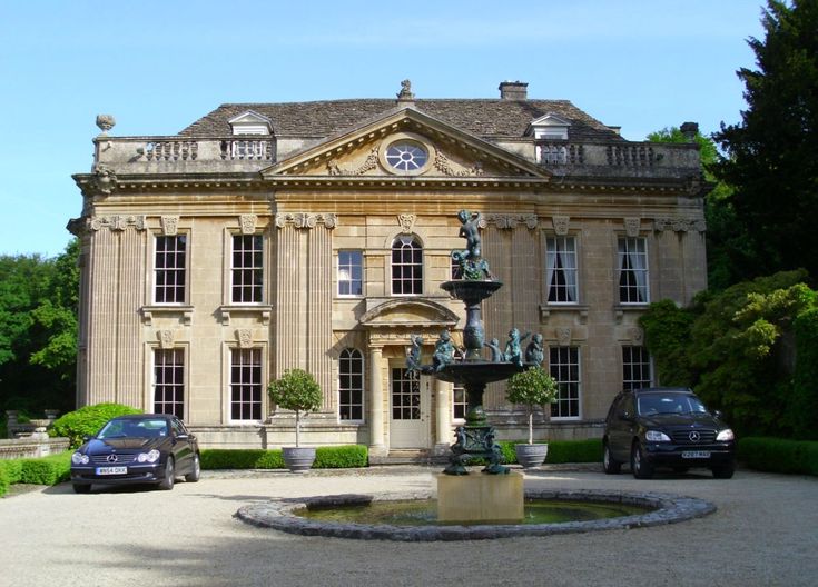 two cars parked in front of a large building with a fountain and statues on it