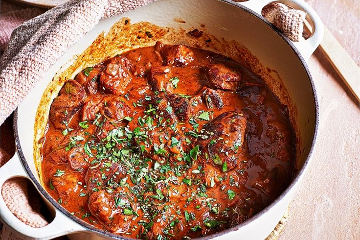 a large pot filled with meat and sauce on top of a wooden table next to a towel