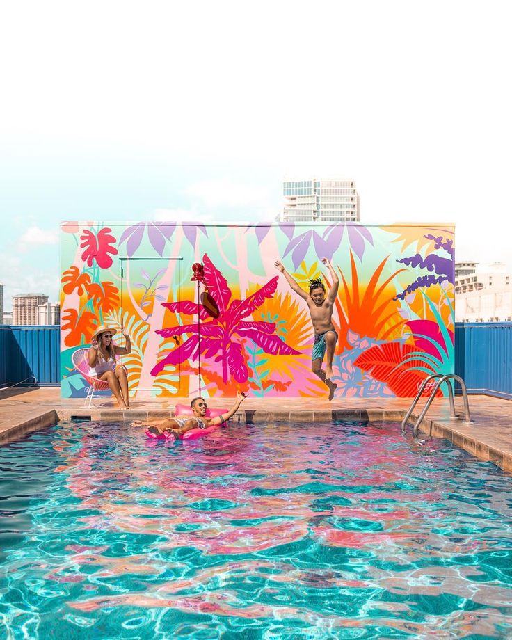 two people are in the pool with colorful paintings on the wall behind them and one person is holding a surfboard