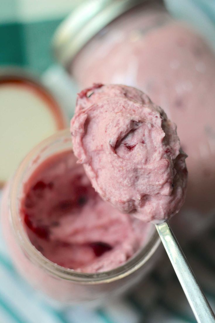 a spoon full of ice cream sitting on top of a jar filled with raspberries