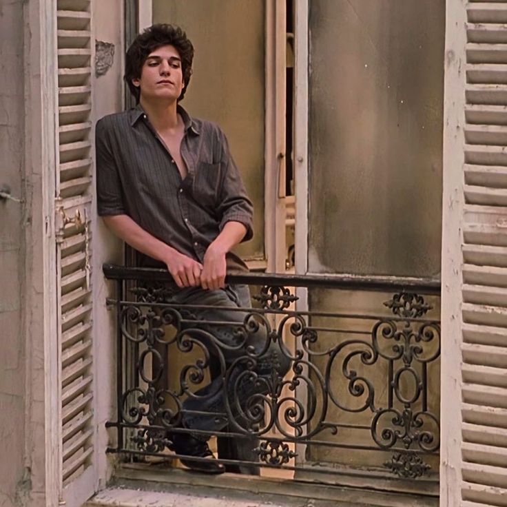 a young man sitting on a balcony looking out the window with his hands in his pockets