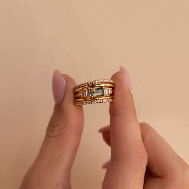 a woman's hand holding two gold rings with diamonds on each one and the other