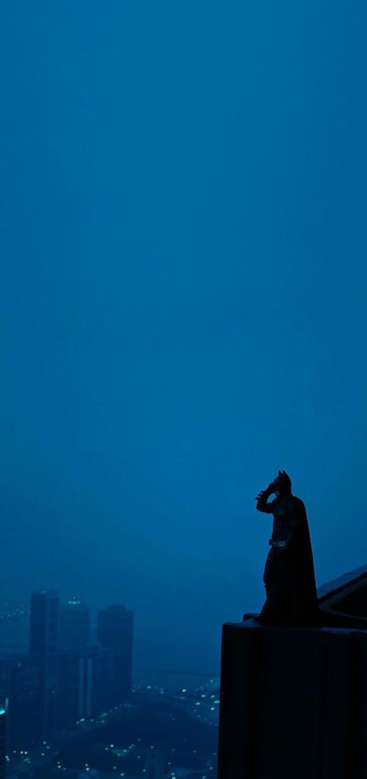 a man standing on top of a building next to a tall clock tower at night