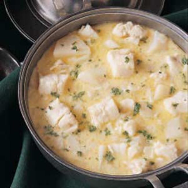 a pan filled with food sitting on top of a green table cloth next to silver spoons