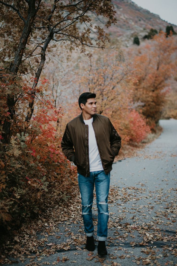 a man standing in the middle of a road surrounded by trees and leaves with his hands on his hips