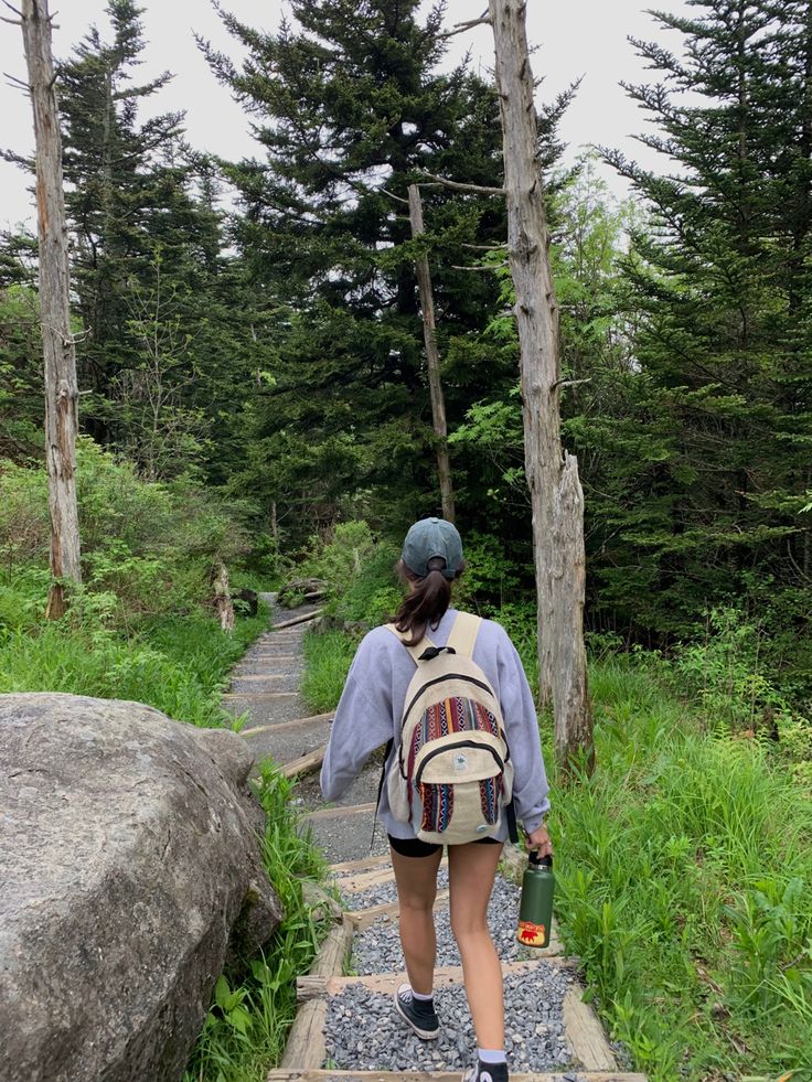 a woman walking up steps in the woods with a backpack on her back, carrying a water bottle