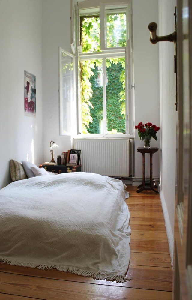 a white bed sitting next to a window on top of a hard wood floored floor