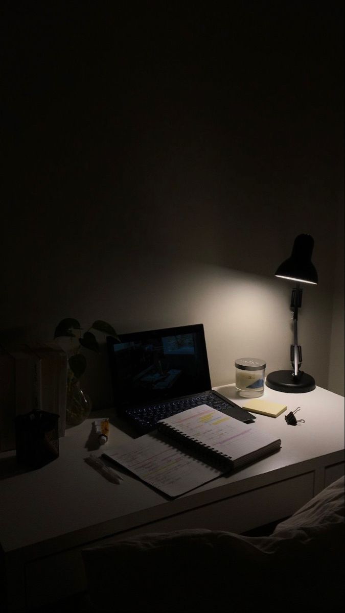 an open laptop computer sitting on top of a desk next to a lamp and papers