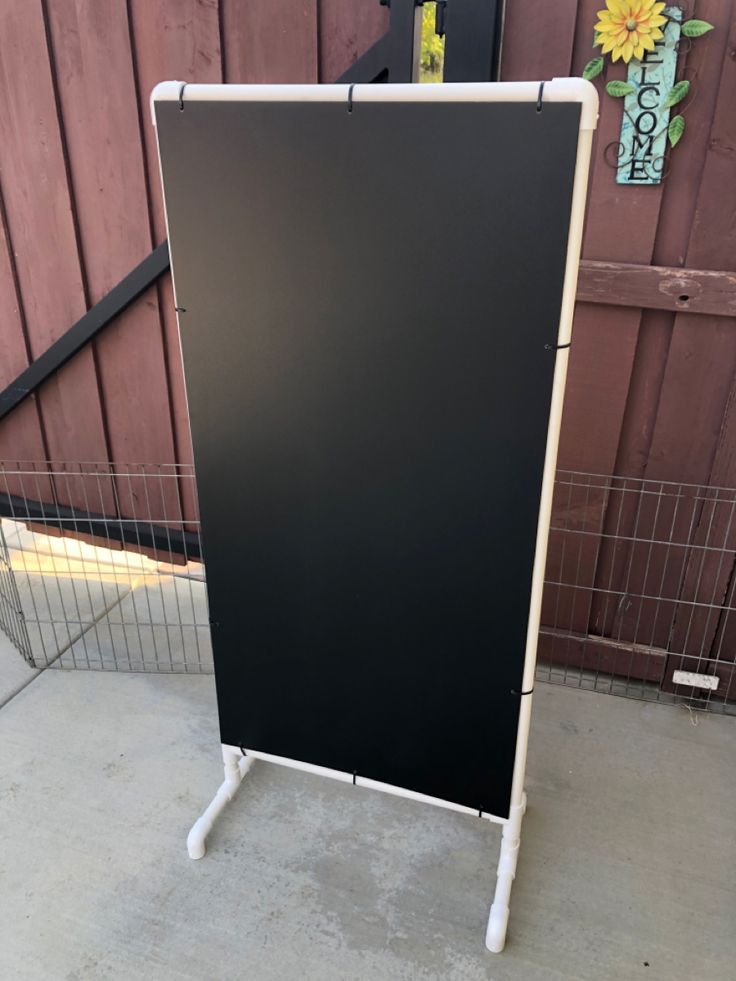 a black and white sign sitting on top of a sidewalk next to a wooden fence