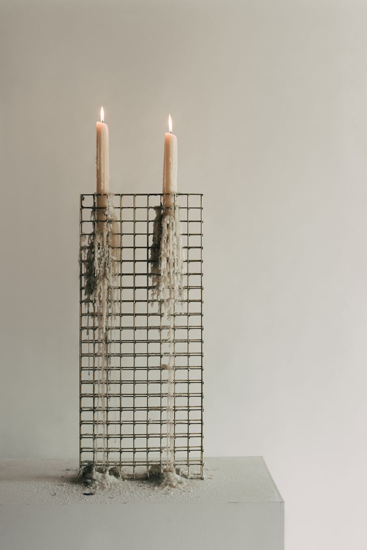 two candles sitting on top of a wire basket with yarn wrapped around it and one candle lit in the middle