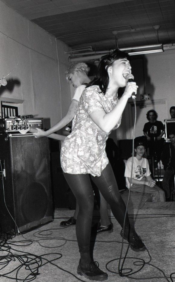 two young women singing into microphones in front of a group of people on stage