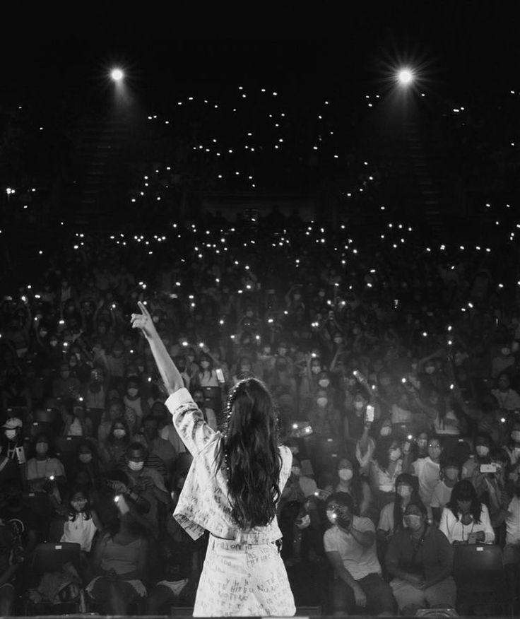 a woman standing on top of a stage holding her arms up in front of an audience