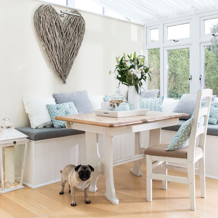 a pug dog standing in front of a table with chairs and pillows on it