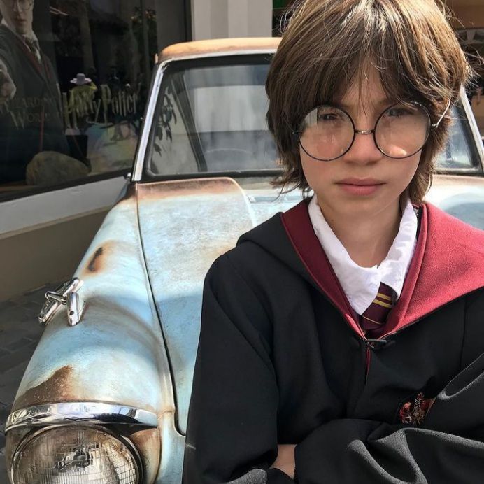 a young boy wearing glasses standing next to an old car