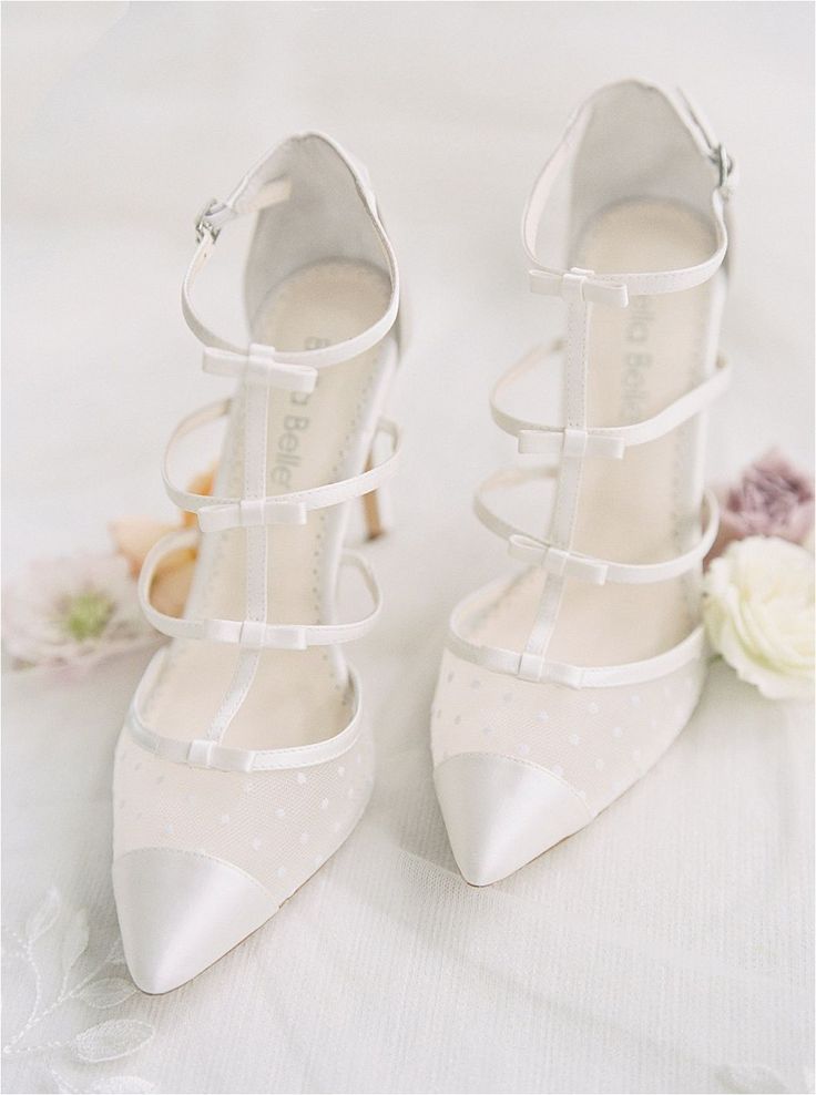 a pair of white shoes sitting on top of a bed next to a bouquet of flowers