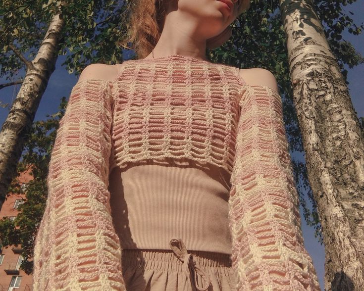 a woman standing in front of two trees wearing a pink sweater and matching shorts with her hair pulled back