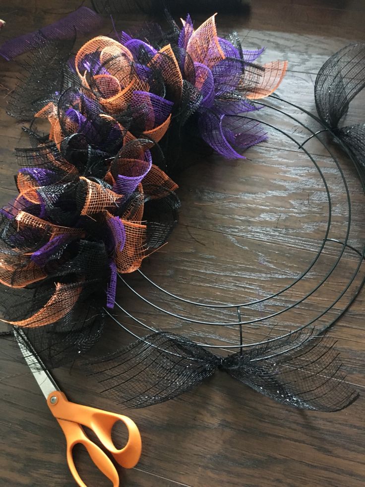 a pair of scissors sitting on top of a table next to a wreath with purple and orange ribbons