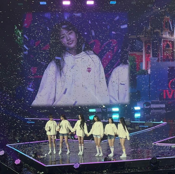 the girls are performing on stage in front of a large screen