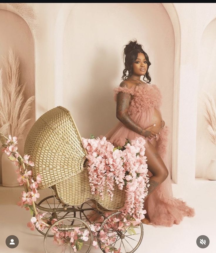 a woman in a pink dress sitting next to a baby carriage with flowers on it