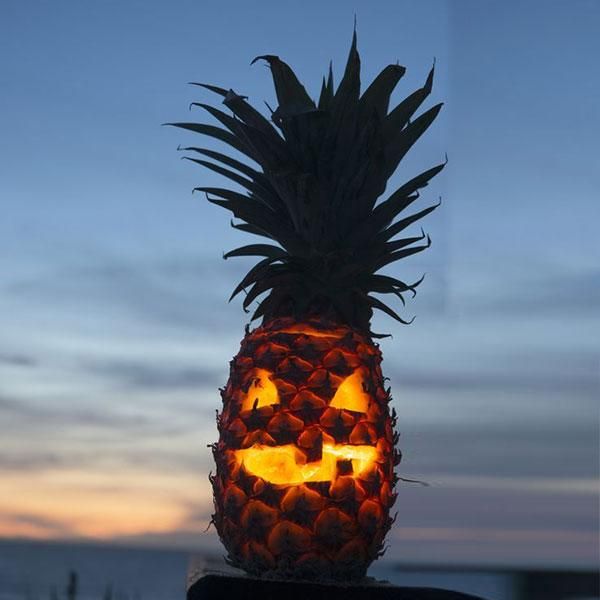 a lit up pineapple sitting on top of a wooden table next to the ocean