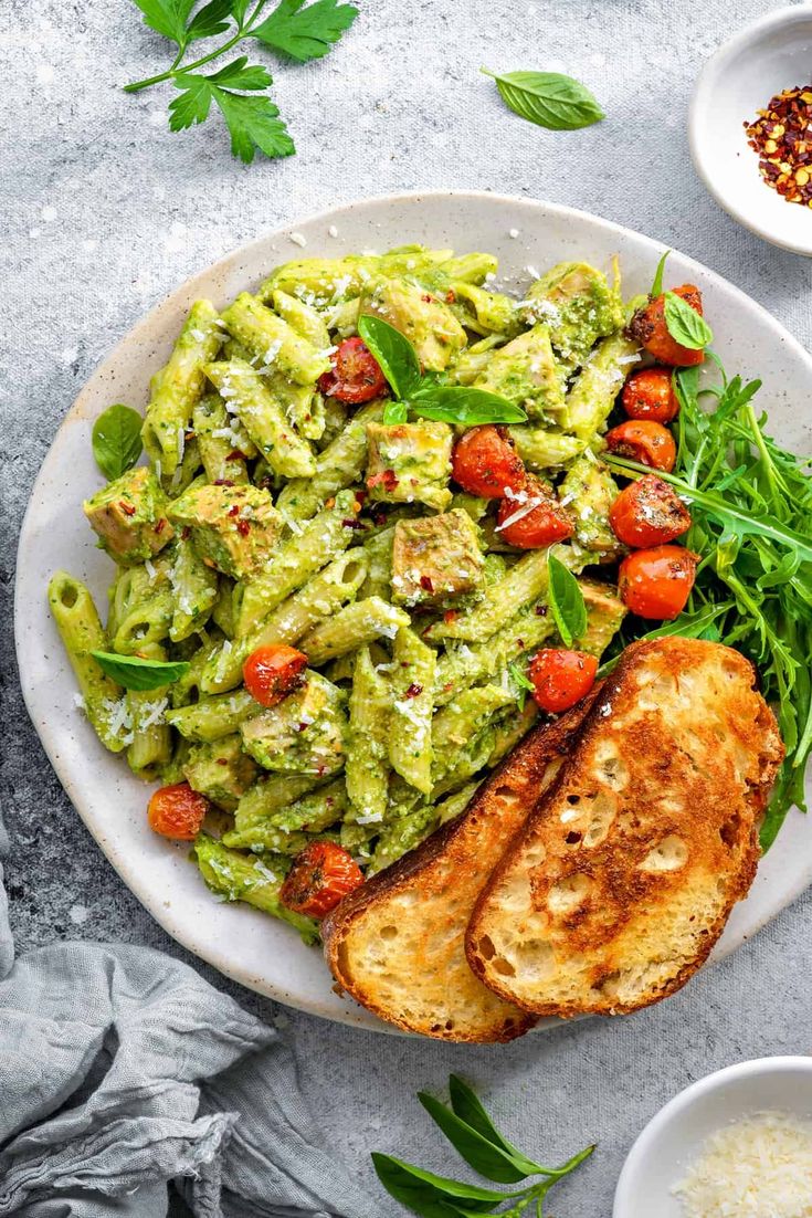 a white plate topped with pasta and pesto covered chicken next to other plates of food