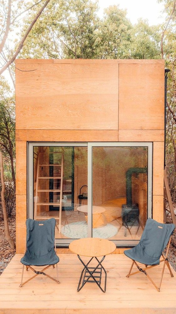 two chairs and a table in front of a small wooden cabin with sliding glass doors