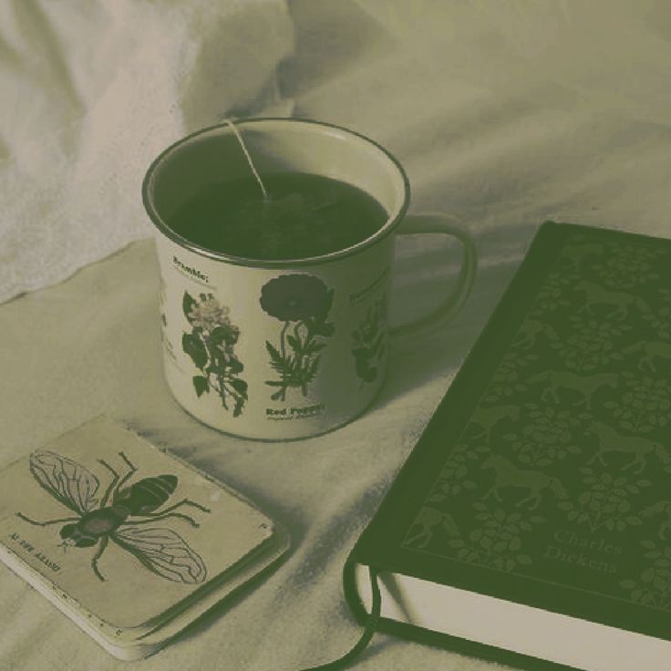 a book and candle on a bed next to a cup with a tea in it