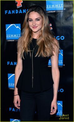 a woman with long hair standing in front of a blue background and wearing black pants