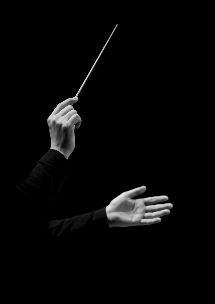 a person holding a conductor's baton in the dark with their hands extended out