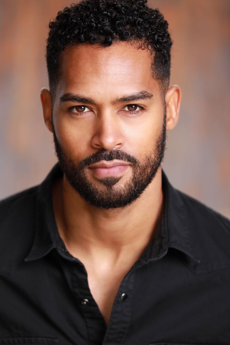 a close up of a person with a beard and black shirt in front of a brown background