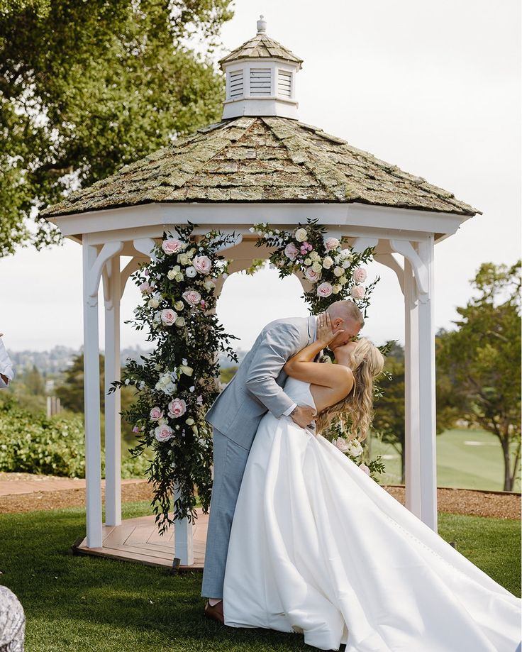 a bride and groom kissing in front of a gazebo at their outdoor wedding ceremony