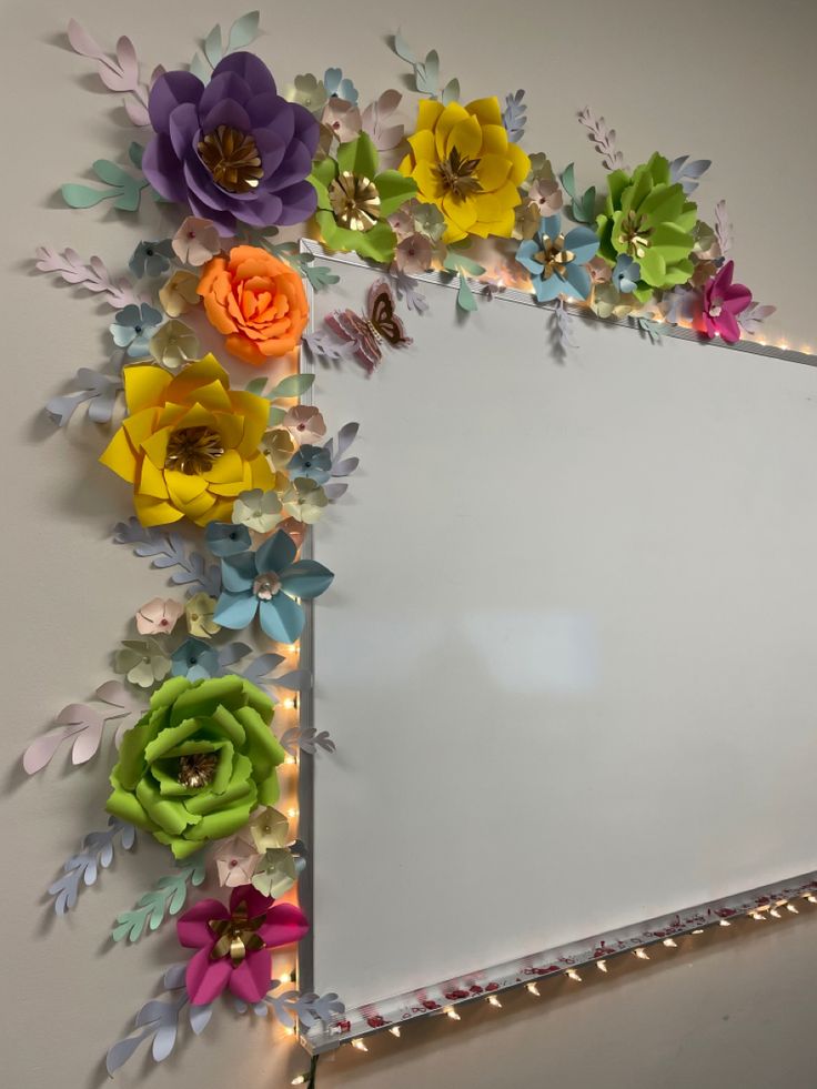 a mirror with paper flowers on it and lights around the edges that are lit up