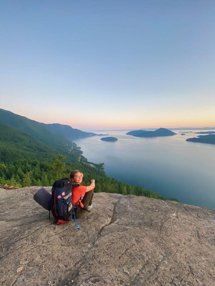 a man sitting on top of a large rock next to a body of water in the distance