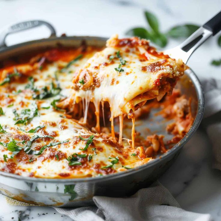 a slice of lasagna being lifted from a skillet with cheese and sauce