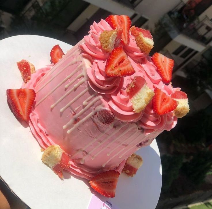 a cake with pink frosting and strawberries on top is being held by someone