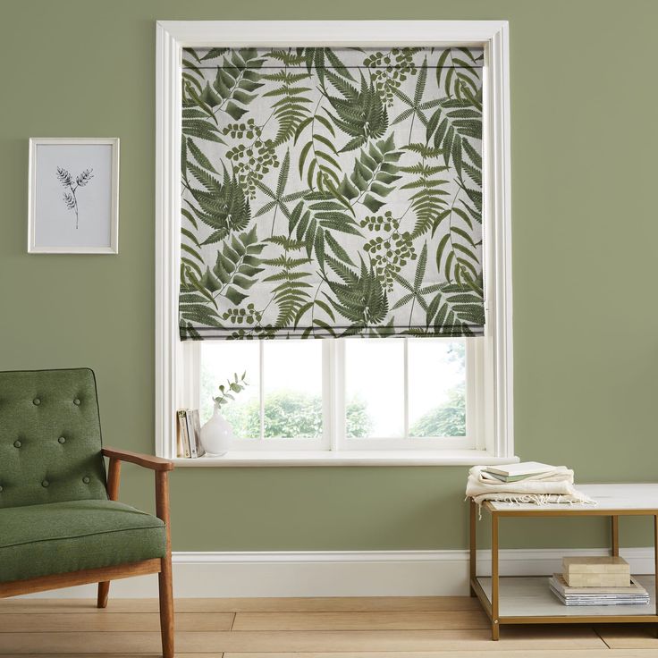 a green chair sitting in front of a window covered in leafy roman blind shades