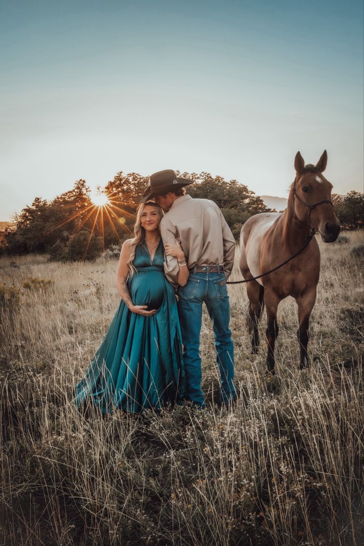 a pregnant woman standing next to a man in a field with a horse behind her