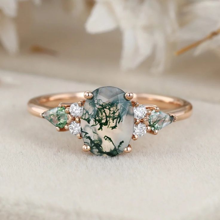 an image of a ring with green and white stones in it on top of a cloth