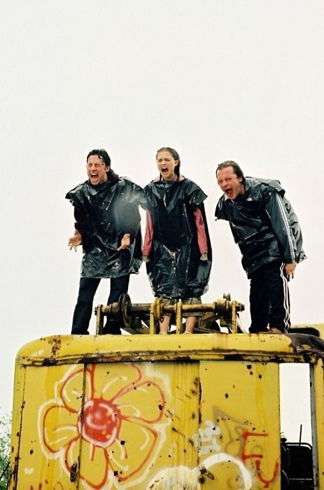 three men standing on top of a yellow truck with graffiti painted on it's side